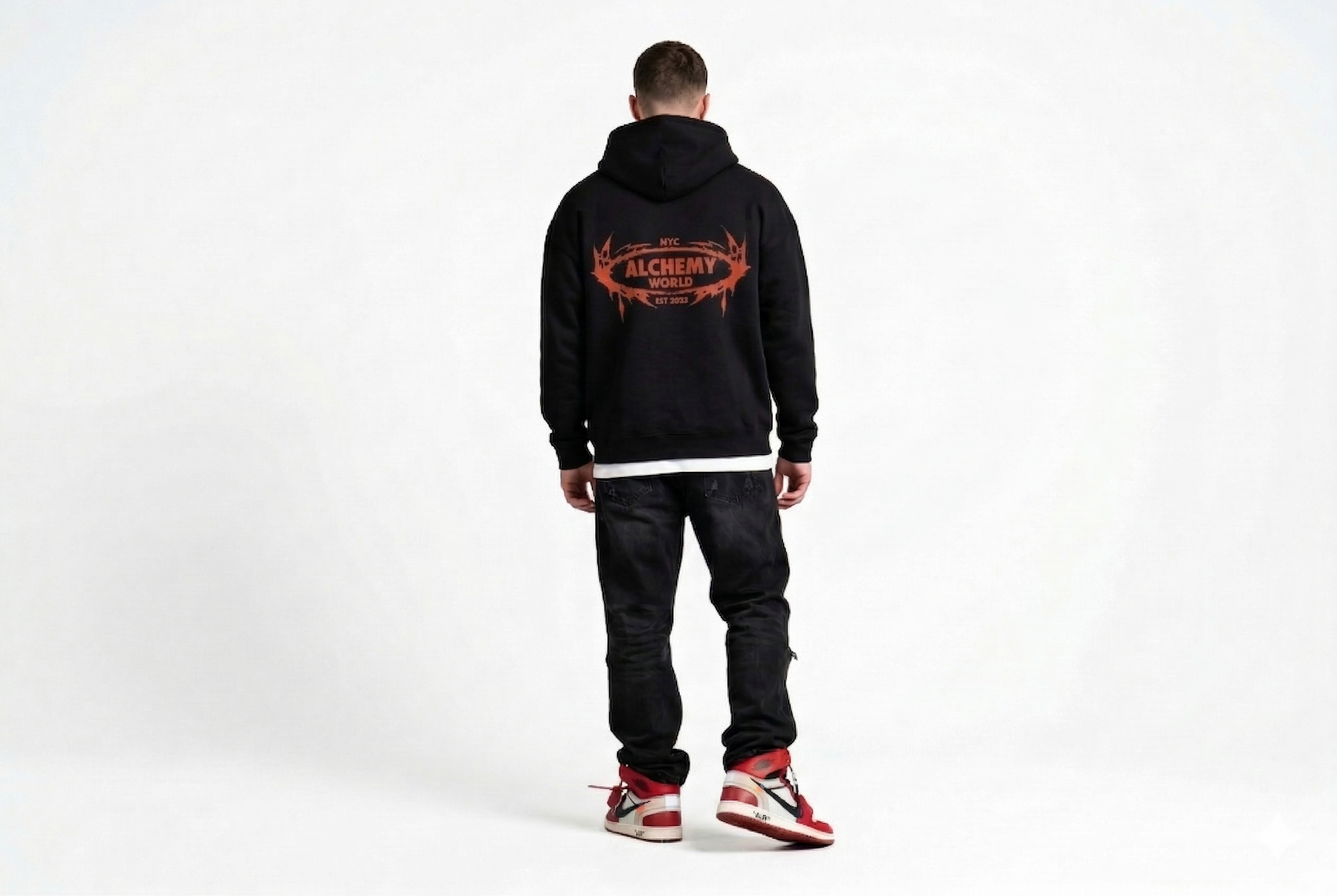 Person wearing a black hoodie with a visible brand logo on the back, standing against a white background.